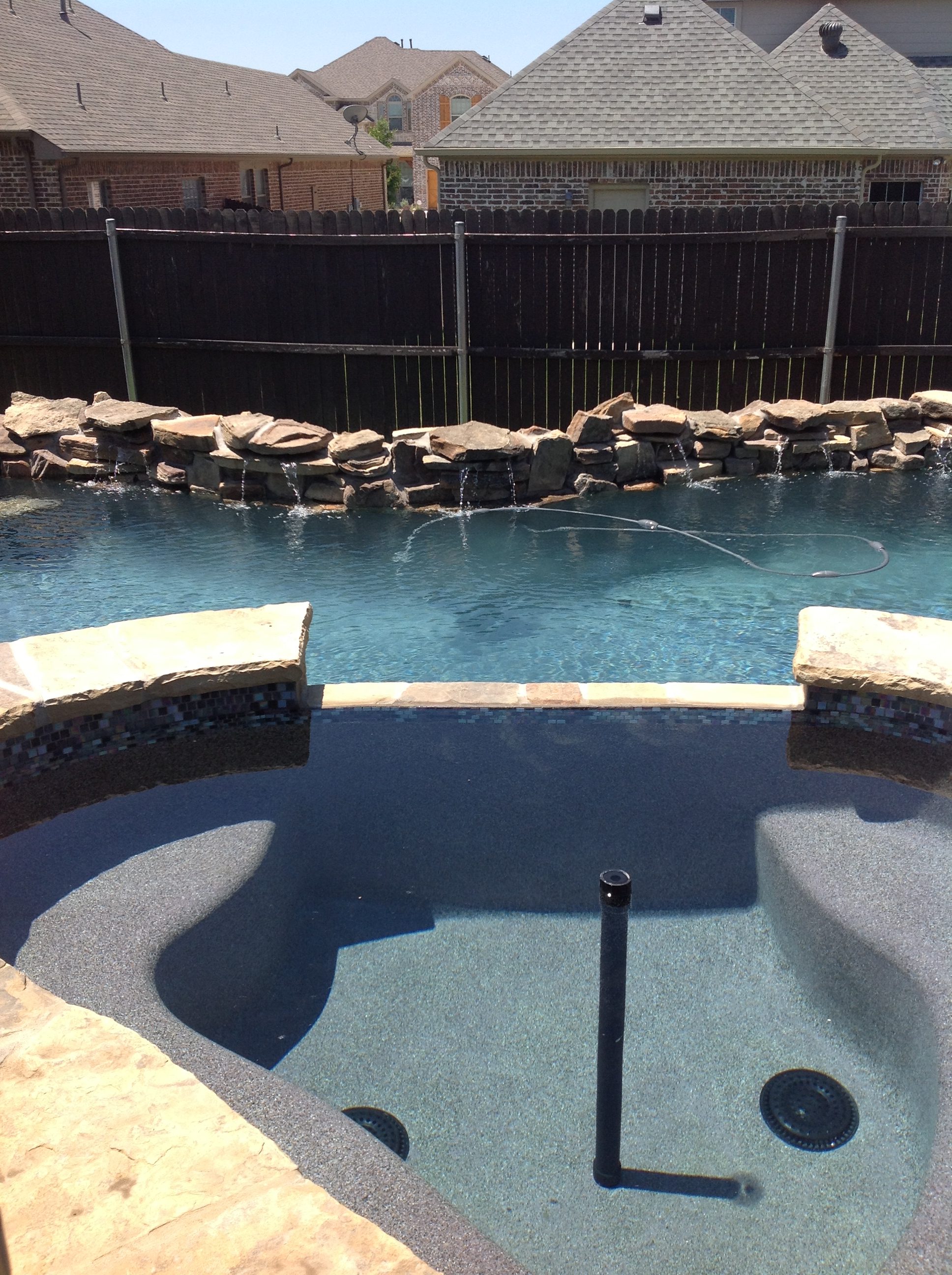 A pool with a large stone wall and a hot tub.